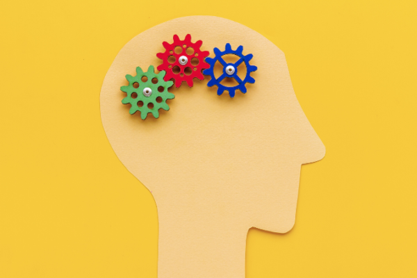 A yellow background with a paper cutout of a human head with gears turning over the brain area.
